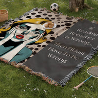 The blanket is being displayed as a picnic blanket in a park setting with a tree stump, picnic basket, plate of muffins, and a tennis racquet and a soccer ball lying around.
