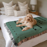 The blanket is displayed neatly folded on a bed with a white bedspread and striped pillows and a large white dog laying on it.