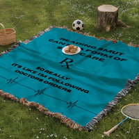The blanket is being displayed as a picnic blanket in a park setting with a tree stump, picnic basket, plate of muffins, and a tennis racquet and a soccer ball lying around.

