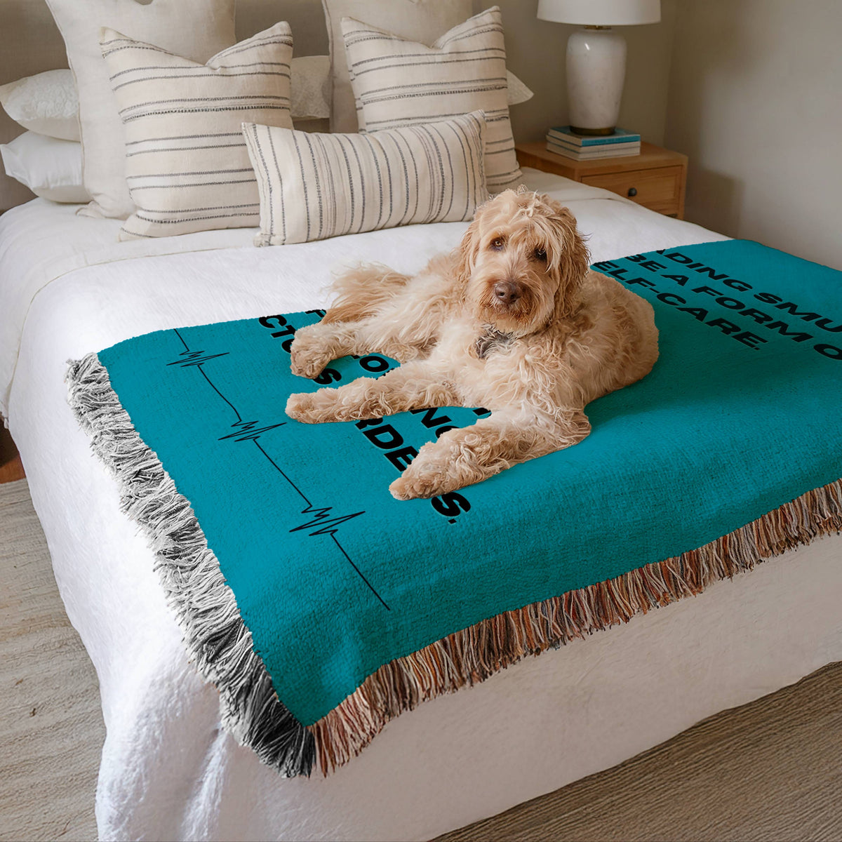 The blanket is displayed neatly folded on a bed with a white bedspread and striped pillows and a large white dog lying on it.

