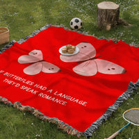 The blanket is being displayed as a picnic blanket in a park setting with a tree stump, picnic basket, plate of muffins, and a tennis racquet and a soccer ball lying around.
