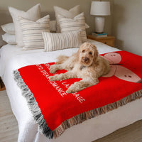 The blanket is displayed neatly folded on a bed with a white bedspread and striped pillows and a large white dog laying on it.
