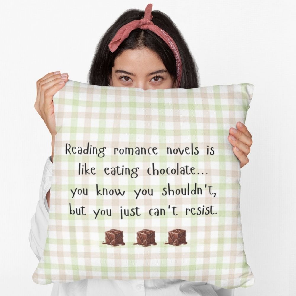 A woman is holding the square pillow with a beige , pink and green plaid background. Black playful text says: “Reading romance novels is like eating chocolate… you know you shouldn’t, but you just can’t resist.” Three illustrated chocolate pieces sit along the bottom. A cheeky decorative pillow for romance readers.