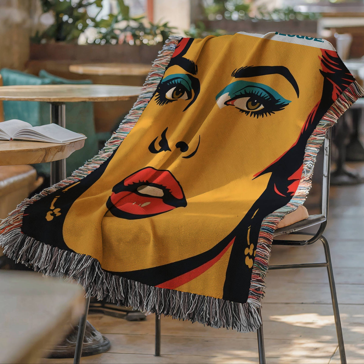 Retro pop art woven blanket draped over a café chair beside an open book and coffee cup, perfect for romance readers and cozy reading spaces.