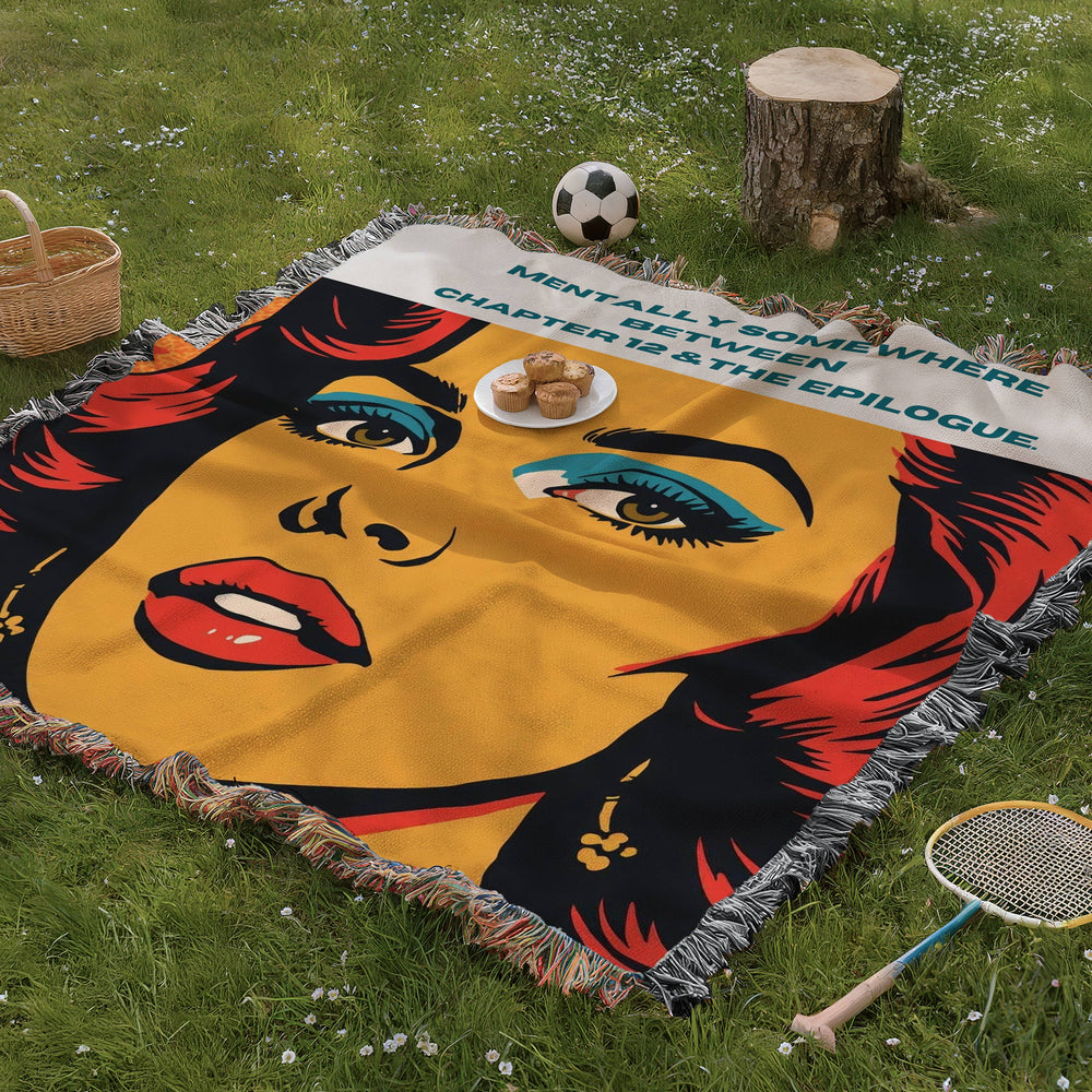 Funny romance reader woven blanket displayed on grass in a picnic setting featuring bold pop art artwork and bookish humor with the phrase: "Mentally Somewhere Between Chapter 12 & The Epilogue,".