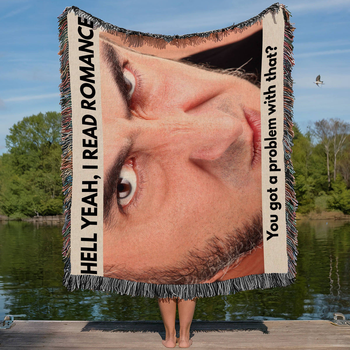 Funny woven blanket featuring an angry man's face and the phrase Hell Yeah I Read Romance displayed by a person holding it outdoors on a dock.