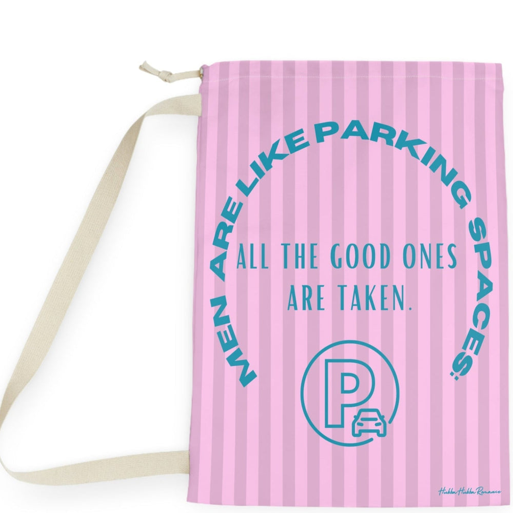 This laundry bag features a pink background with vertical pastel-pink stripes. Centered, bold, teal text reads: "All the good ones are taken." Above the text, in a large curved arc, it says: “Men are like parking spaces!” Below the quote is a parking symbol: a capital letter “P” inside a circle with a car icon in the corner. The bag includes a drawstring closure and a canvas carrying strap. The tone is playful, retro, and full of tongue-in-cheek charm. It is the large version.