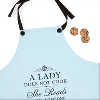 A light blue kitchen apron with black neck and waist straps, featuring the printed text 'A LADY DOES NOT COOK. She Reads WHILE SOMEONE' in dark navy lettering.