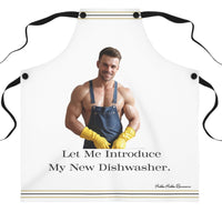 The apron features an image of a muscular, shirtless man wearing denim overalls, yellow rubber gloves, and smiling. Below the image, the text reads: "Let Me Introduce My New Dishwasher." The apron has thin black and gold stripes along the top and bottom edges. The background includes white shelves, cutting boards, and kitchen items.
