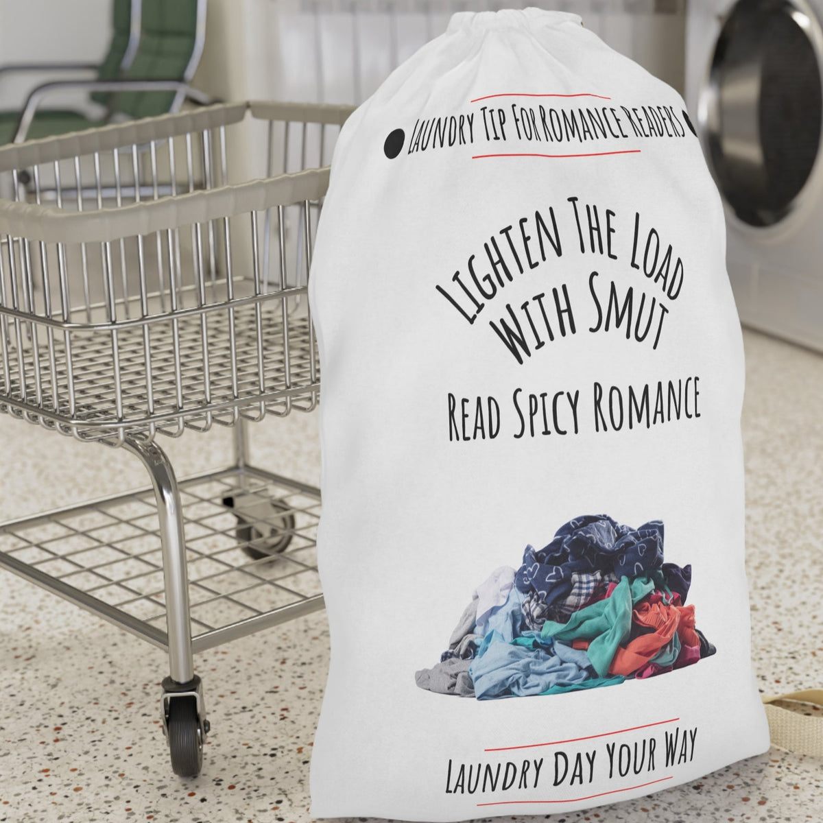 This laundry bag features a white background with a colorful pile of clothes at the bottom. Above the pile, black text reads: “Lighten the Load with Smut” in an arched layout. Below that, in a straight line, it says: “Read Spicy Romance.” At the top, the header “Laundry Tip for Romance Readers” is centered between two black dots and underlined in red. The bottom of the image reads: “Laundry Day Your Way” in black text, also underlined in red. The bag includes a drawstring closure and a canvas carry strap.