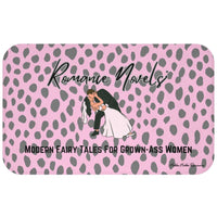 ADA Product Description:
This bath mat features a light pink background with a gray leopard print pattern. Centered near the top is the text “Romance Novels” in a black script font. Below that is an illustrated image of a groom dipping a bride into a dramatic kiss. At the bottom, bold black text reads: “Modern Fairy Tales For Grown-Ass Women.” The mat is soft and absorbent, combining playful design with a bold celebration of the romance genre. This is the larger version.
