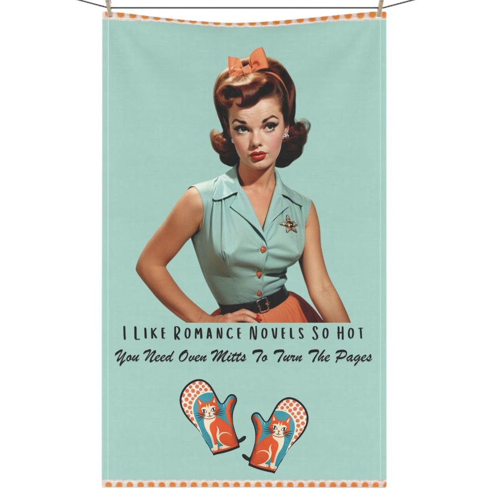 The kitchen towel features a vintage-inspired illustration of a glamorous woman from the 1950s, sporting a stylish updo and a mint green camp shirt, black belt, and an orange skirt, accompanied by text that reads, "I Like Romance Novels So Hot You Need Oven Mitts to Turn the Pages." Below the text are two whimsical oven mitts with playful cats and orange polka-dot details. The design combines retro charm and humor, appealing to fans of steamy romance novels. The napkin is displayed on a clothesline.