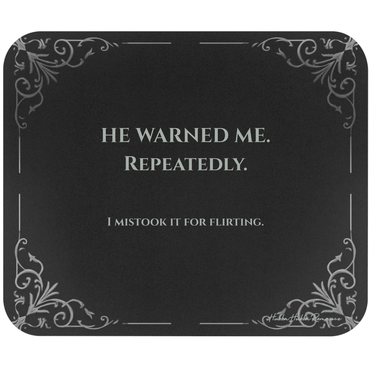 A rectangular black mouse pad with rounded corners, featuring light grey text and light gray filigree corner accents. The text  reads 'HE WARNED ME. REPEATEDLY. I mistook it for flirting.