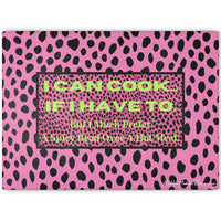 Glass cutting board featuring a hot pink and black leopard print background. Centered on the board is a bold text box that reads: “I CAN COOK—IF I HAVE TO. But I Much Prefer A Spicy Read Over A Hot Meal.” Made from durable, textured tempered glass with non-slip rubber feet for stability. This is the larger size.
