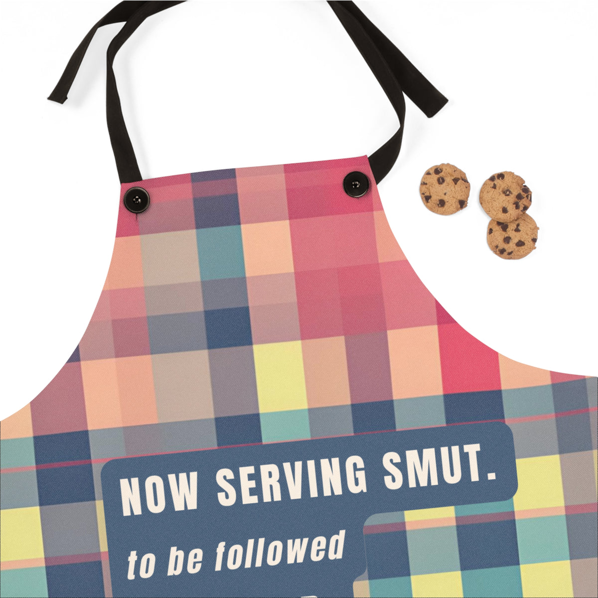 A novelty kitchen apron with a colorful plaid pattern and black neck strap, featuring the text 'NOW SERVING SMUT. to be followed' on the lower front.