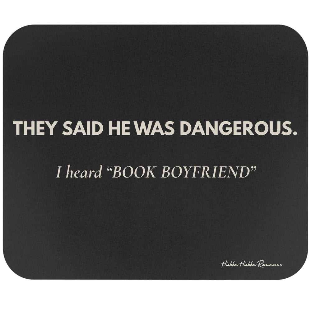 A dark gray rectangular mouse pad with rounded corners featuring the quote 'THEY SAID HE WAS DANGEROUS. I heard ‘BOOK BOYFRIEND’' in cream text.