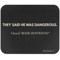 A dark gray rectangular mouse pad with rounded corners featuring the quote 'THEY SAID HE WAS DANGEROUS. I heard ‘BOOK BOYFRIEND’' in cream text.