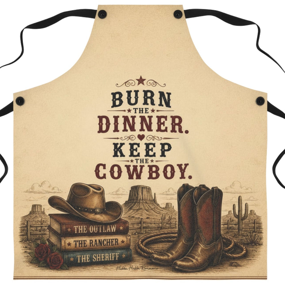 A beige apron with black neck and waist ties, featuring a western-themed graphic print with the text 'BURN THE DINNER. KEEP THE COWBOY.