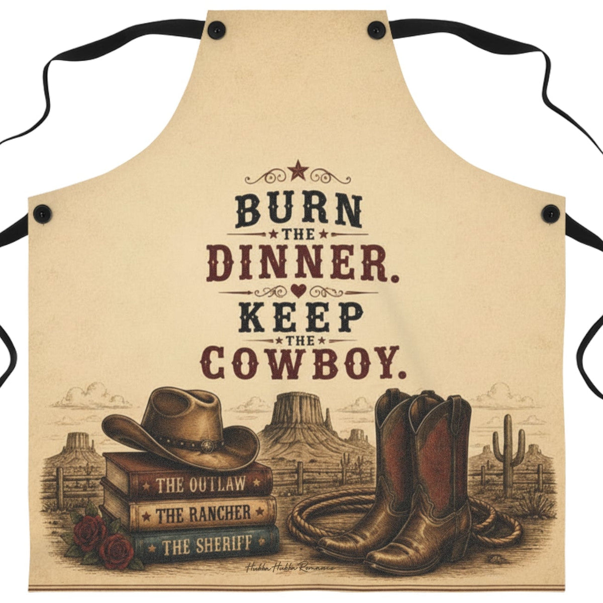 A beige apron with black neck and waist ties, featuring a western-themed graphic print with the text 'BURN THE DINNER. KEEP THE COWBOY.