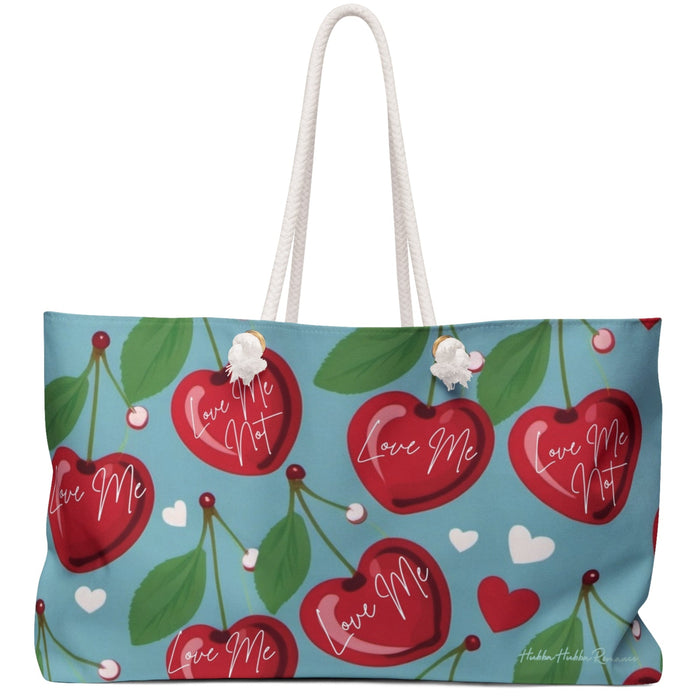 Weekender bag with teal background, cherry and heart pattern, and alternating text: “Love Me” and “Love Me Not.”