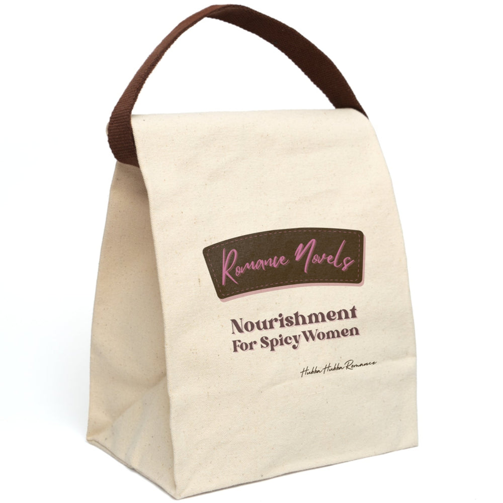 This lunch bag features a plain canvas background with two prominent text sections. At the top, a stylized brown label with pink stitching contains the words “Romance Novels” in a cursive pink font. Below the label, bold pink and brown text reads: “Nourishment For Spicy Women.” The design resembles a vintage food label with a modern, sassy twist. The bag is made of durable canvas with a roll-top closure and a carrying strap, perfect for everyday use and displayed upright in this image.