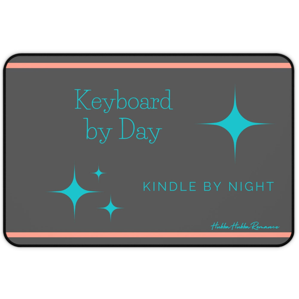 A charcoal gray desk mat features a playful message split across two lines: "Keyboard by Day" in turquoise serif text on the left, and "Kindle by Night" in sans-serif turquoise on the right. Turquoise starburst-style sparkles accent the design, and two thin orange horizontal lines run along the top and bottom edges.