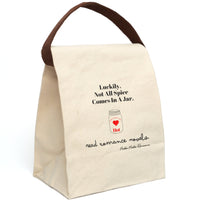 This canvas lunch bag features a natural canvas background with bold black typography. At the top, large black text reads: “Luckily, Not All Spice Comes In A Jar.” Below is a simple drawing of a mason jar with a red heart in the center. At the top of the jar, curved text reads: “Extra Extra Extra,” and beneath the heart, the word “Hot” appears in red. At the bottom of the design, cursive black script reads: “read romance novels.” It has a velcro closing and canvas handle for carrying, displayed upright.
