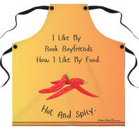 An orangy yellow apron with black straps features the phrase, "I like my book boyfriends how I like my food. Hot and spicy." in black text. Below the text, there is an illustration of three red chili peppers. The bottom of the apron has a decorative striped trim.
