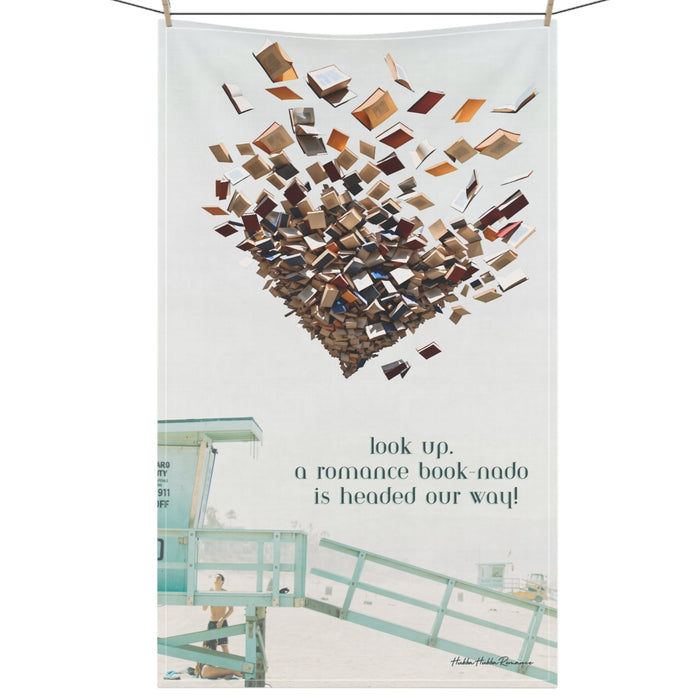 Oversized towel with beach scene, lifeguard tower, and swirling tornado of books in the sky. Text reads: “Look Up. A Romance Book-Nado Is Headed Our Way.”