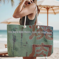 The tote bag is being modeled by a woman in a green tank top, standing on the beach, wearing it over her shoulder.