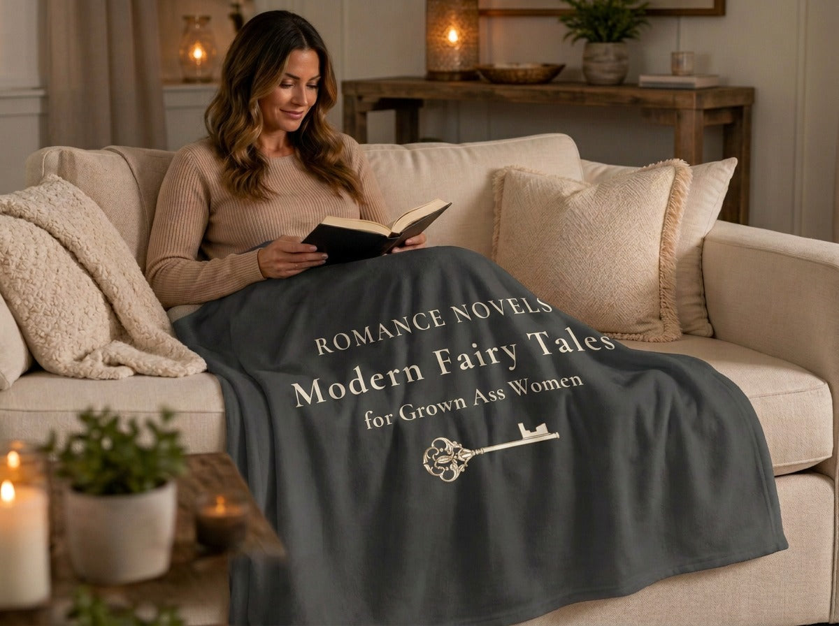 Woman sitting on a couch rading a book. A grey sweatshirt blanket with the words Romance Novels Modern Fairy Taled For Grown Ass Women in light cream text.