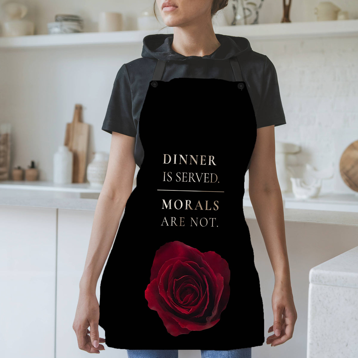 A woman wearing a black apron with a red rose graphic and large cream colored text above it that reads 'DINNER IS SERVED. MORALS ARE NOT.