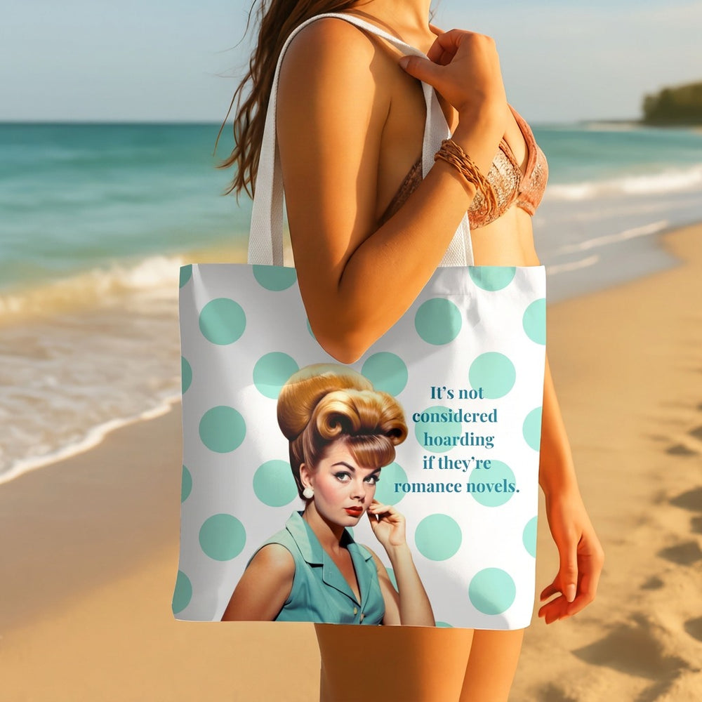 A woman on a beach holds a white tote bag with large mint green polka dots and a vintage-style illustrated woman on the front, next to the text, 'It's not considered hoarding if they're romance novels.'.