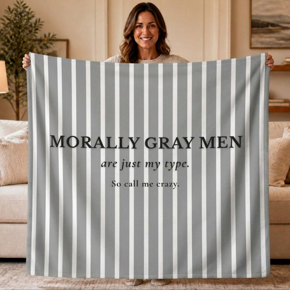 A woman holds up a large gray and white vertically striped sweatshirt blanket with the text 'MORALLY GRAY MEN are just my type. So call me crazy.