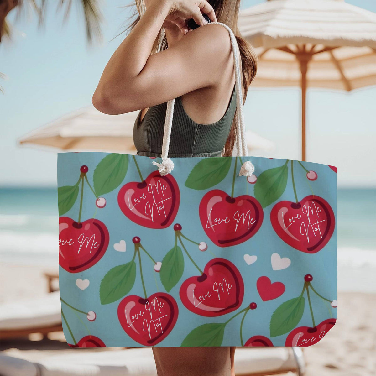 The tote bag is being modeled by a woman in a green tank top, standing on the beach, wearing it over her shoulder.

