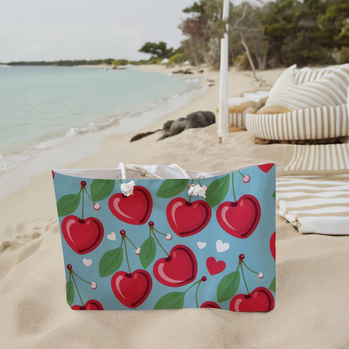 The weekender bag is displayed standing upright on the beach next to beach towels.