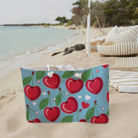 The weekender bag is displayed standing upright on the beach next to beach towels.