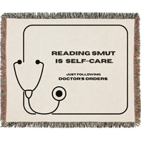 A woven cotton throw blanket with fringed edges, featuring a black stethoscope graphic and the text 'READING SMUT IS SELF-CARE. JUST FOLLOWING DOCTOR'S ORDERS.