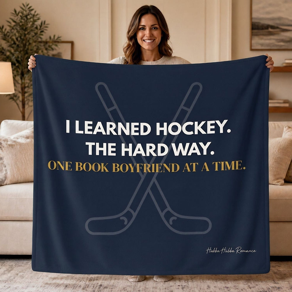 A woman stands in a living room holding a navy blue sweatshirt  blanket that reads, 'I LEARNED HOCKEY. THE HARD WAY. One book boyfriend at a time.