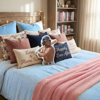 Decorative throw pillow featuring a handsome baseball book boyfriend with dark hair and an athletic build, wearing a batting helmet and holding a baseball bat, shirtless and smiling confidently. Shown styled on a cozy bed with layered pillows, romance-themed accent cushions, and a bookshelf filled with books. This sports romance decorative pillow for romance readers is available in three sizes (10" x 10", 16" x 16", and 22" x 22") for beds, couches, and reading chairs.