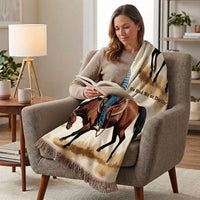 A woman sits in a gray armchair reading a book, wrapped in a cream throw blanket featuring a brown horse illustration and the text 'He Had Me at Darlin''.