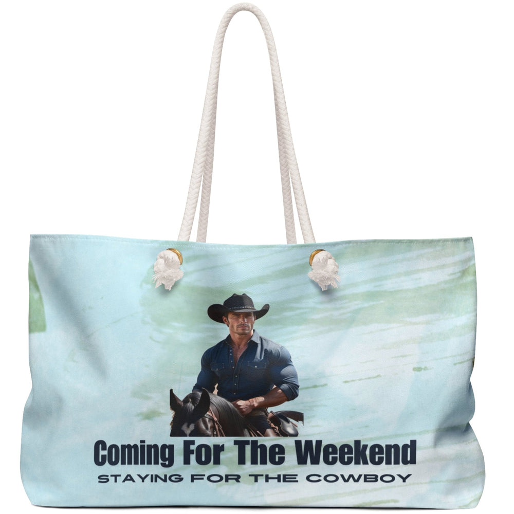 Image shows a muscular cowboy in a dark blue button-down and black hat riding a black horse against a soft watercolor sky blue background. Below the image is bold black text reading: “Coming for the Weekend,” followed by smaller, italicized text: “Staying for the Cowboy.” The design evokes a western romance aesthetic, blending humor and heat. Displayed on a weekender bag, it targets romance readers who adore cowboy tropes, rugged heroes, and a little weekend mischief.