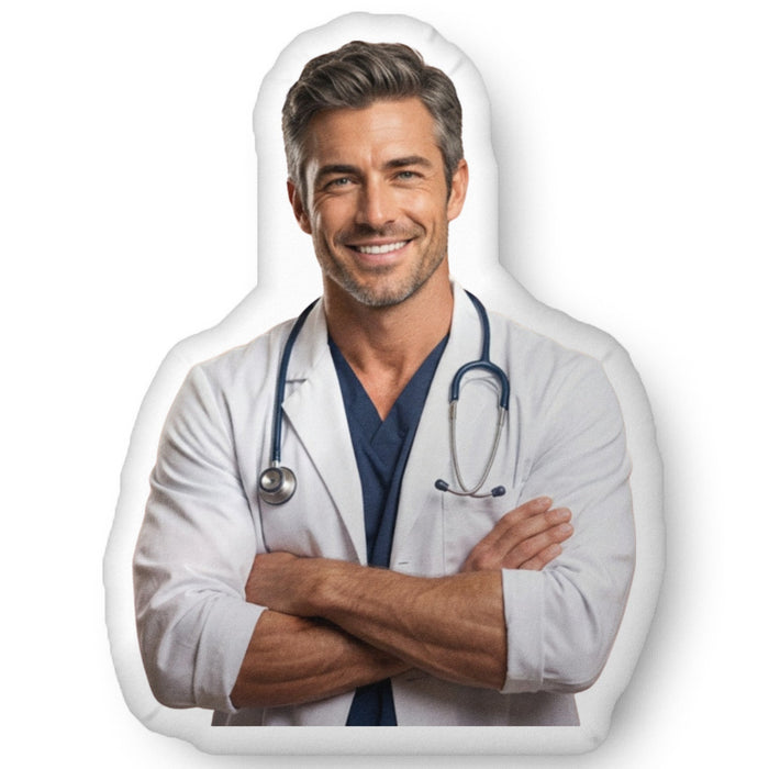 Custom-shaped decorative pillow featuring The Doctor, a handsome medical romance book boyfriend with salt-and-pepper hair, light stubble, and a confident smile, wearing a white lab coat with a stethoscope and folded arms. Shown as a standalone pillow against a neutral background. This medical romance book boyfriend pillow is available in three sizes (10" x 10", 16" x 16", and 22" x 22").