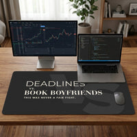 A largecharcoal desk mat with the text 'DEADLINES vs. BOOK BOYFRIENDS.  laptop and adjavent free standing monitor indicate the mat size uitability.