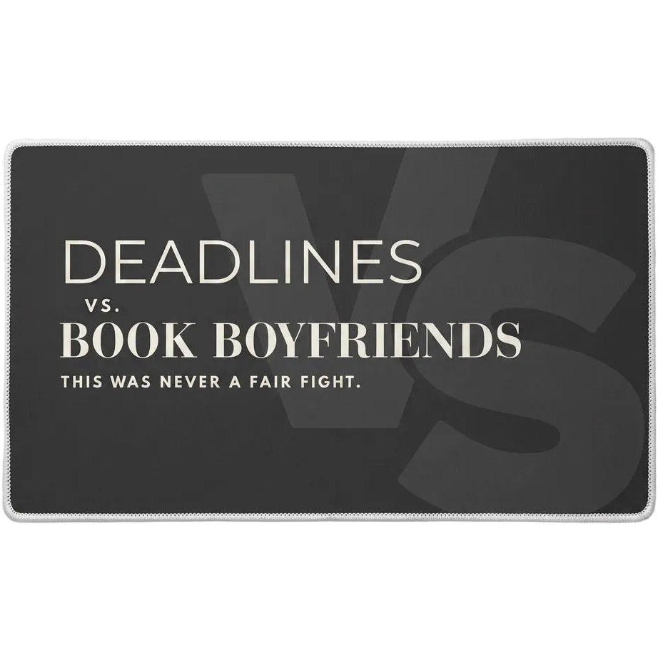 A rectangular charcoal desk mat with cream text reading 'DEADLINES vs. BOOK BOYFRIENDS THIS WAS NEVER A FAIR FIGHT.