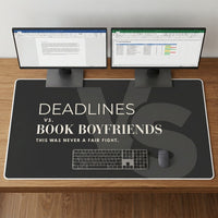 A large charcoal desk mat with the text 'DEADLINES vs. BOOK BOYFRIENDS' and 'THIS WAS NEVER A FAIR FIGHT in cream text.