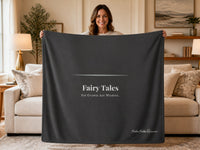 Woman holding a dark charcoal sweatshirt blanket featuring the phrase "Fairy Tales for Grown Ass Women" in a cozy living room. Reading blanket designed for romance readers and fans of modern fairy-tale love stories.