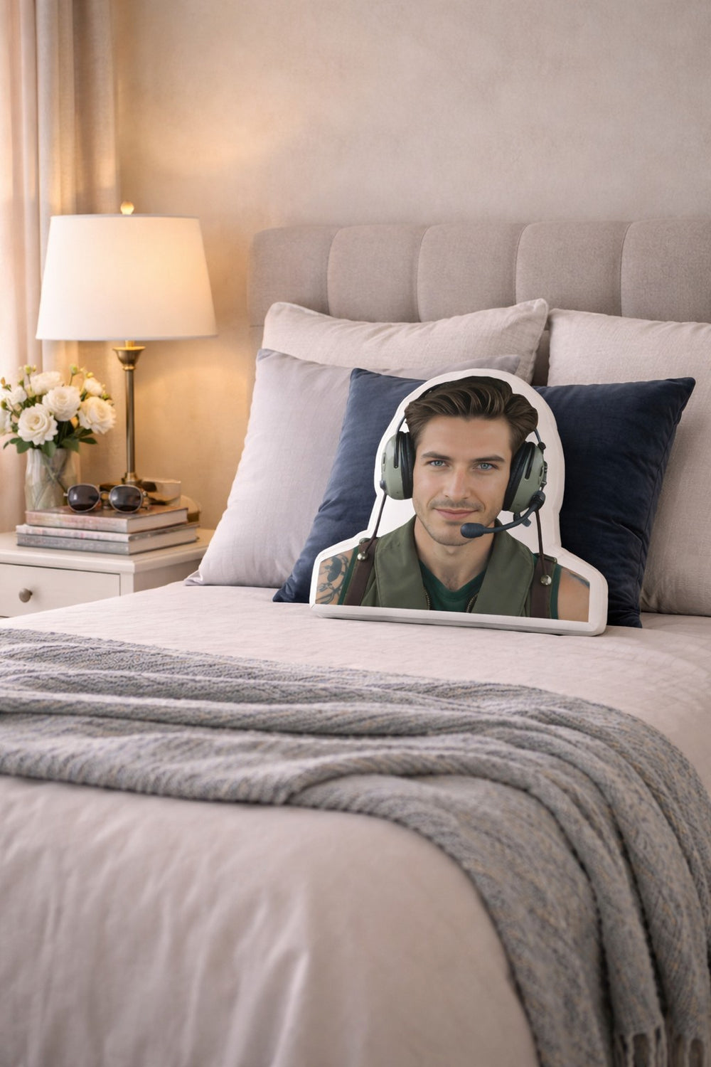 The Fighter Pilot military romance book boyfriend pillow styled on a softly made bed in a feminine, modern bedroom with a light upholstered headboard, crisp neutral bedding, accent pillows, and warm bedside lighting. The scene includes subtle aviation-inspired details and cozy textures, creating a space designed for women who love studly fighter pilot heroes and military romance novels.