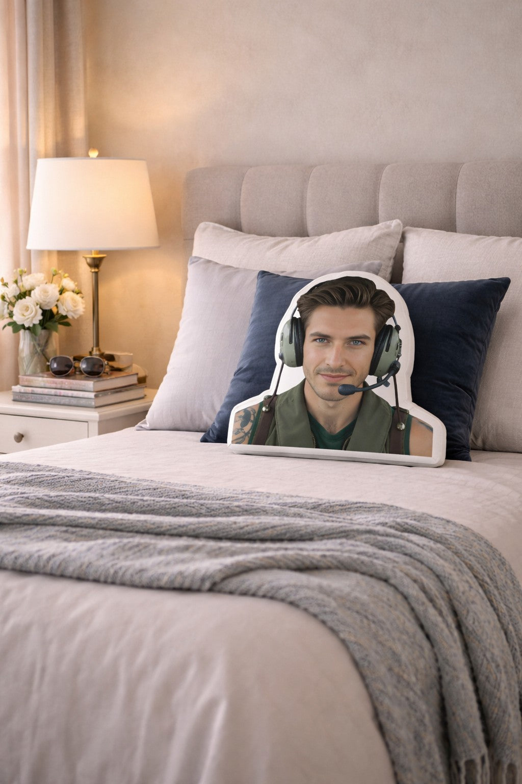 The Fighter Pilot military romance book boyfriend pillow styled on a softly made bed in a feminine, modern bedroom with a light upholstered headboard, crisp neutral bedding, accent pillows, and warm bedside lighting. The scene includes subtle aviation-inspired details and cozy textures, creating a space designed for women who love studly fighter pilot heroes and military romance novels.