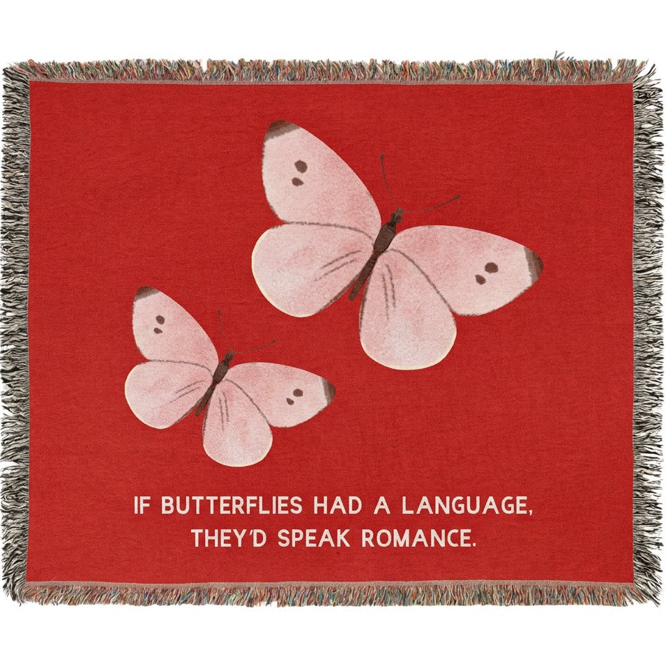 A woven cotton  throw blanket with fringed edges, featuring a bright red background, two pale pink butterflies, and the text 'IF BUTTERFLIES HAD A LANGUAGE, THEY'D SPEAK ROMANCE.' in white at the bottom.